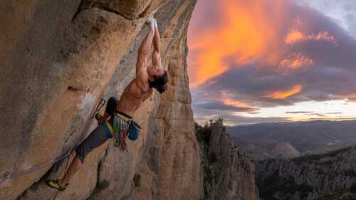Escalador en una pared de roca dramática en las montañas españolas con iluminación naranja y púrpura