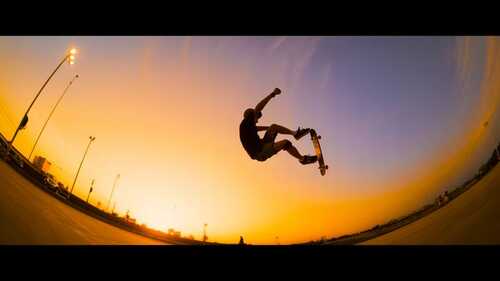 Deportista realizando un truco aéreo de skateboarding al atardecer con cielo naranja y púrpura