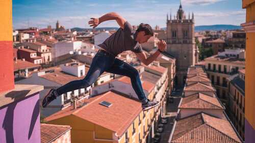 Atleta de parkour saltando entre edificios en una ciudad española con techos de terracota