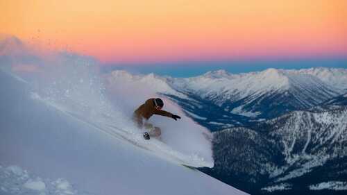 Snowboarder realizando un truco aéreo en montañas nevadas estilo Sierra Nevada con cielo dramático